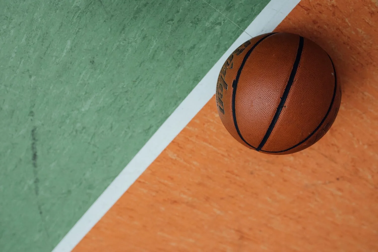 A basketball resting on a painted court at the boundary line between two colored sections