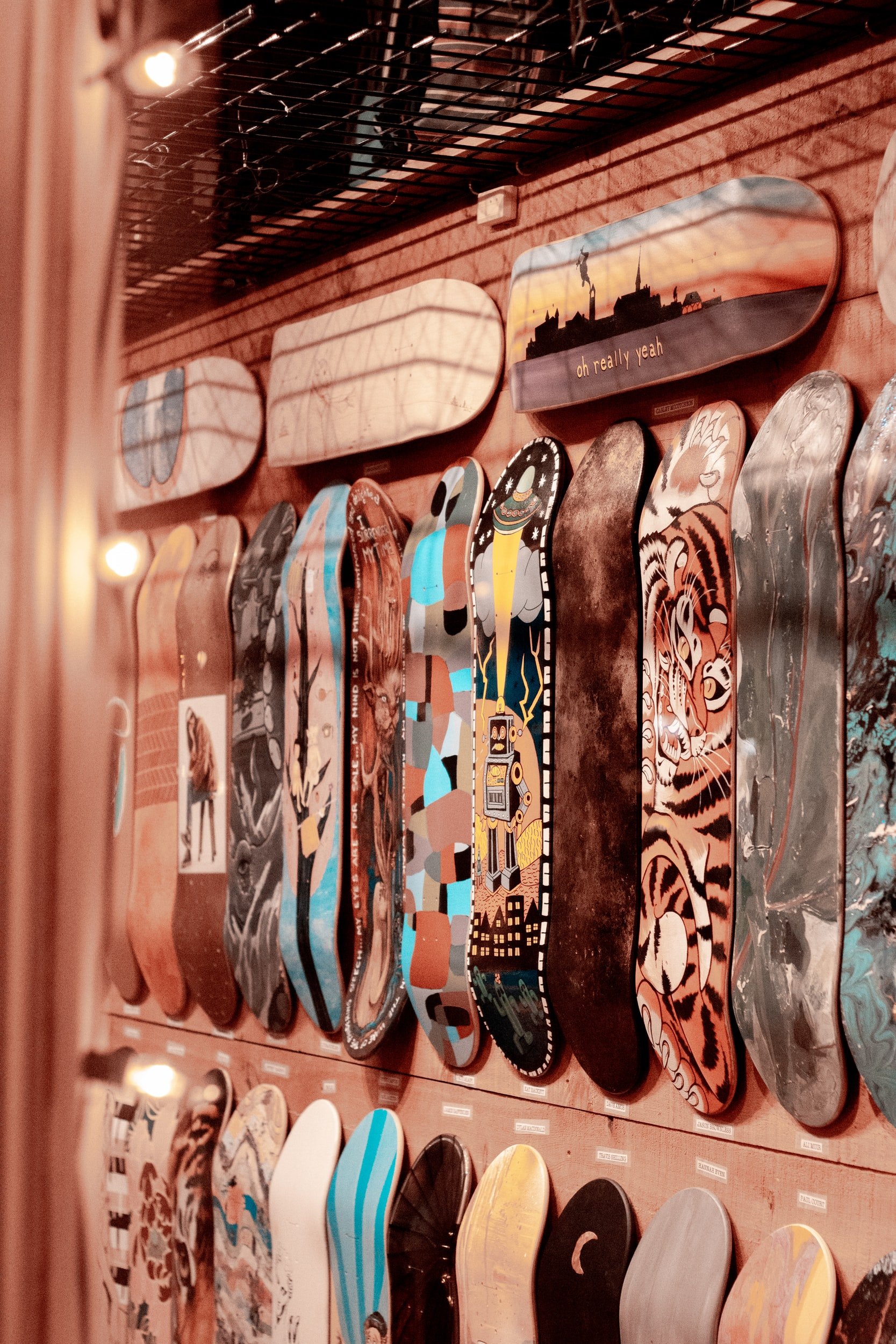 A display rack of skateboard decks featuring various colorful and artistic designs, arranged vertically against a wooden wall.