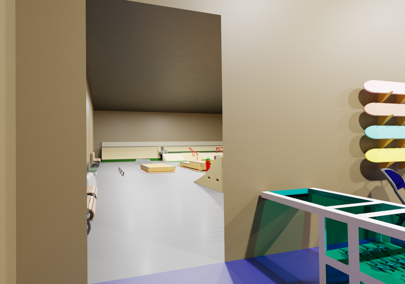 Indoor skate park with ramps, rails, and skateboards, viewed through an open door with colorful skateboards mounted on the wall.