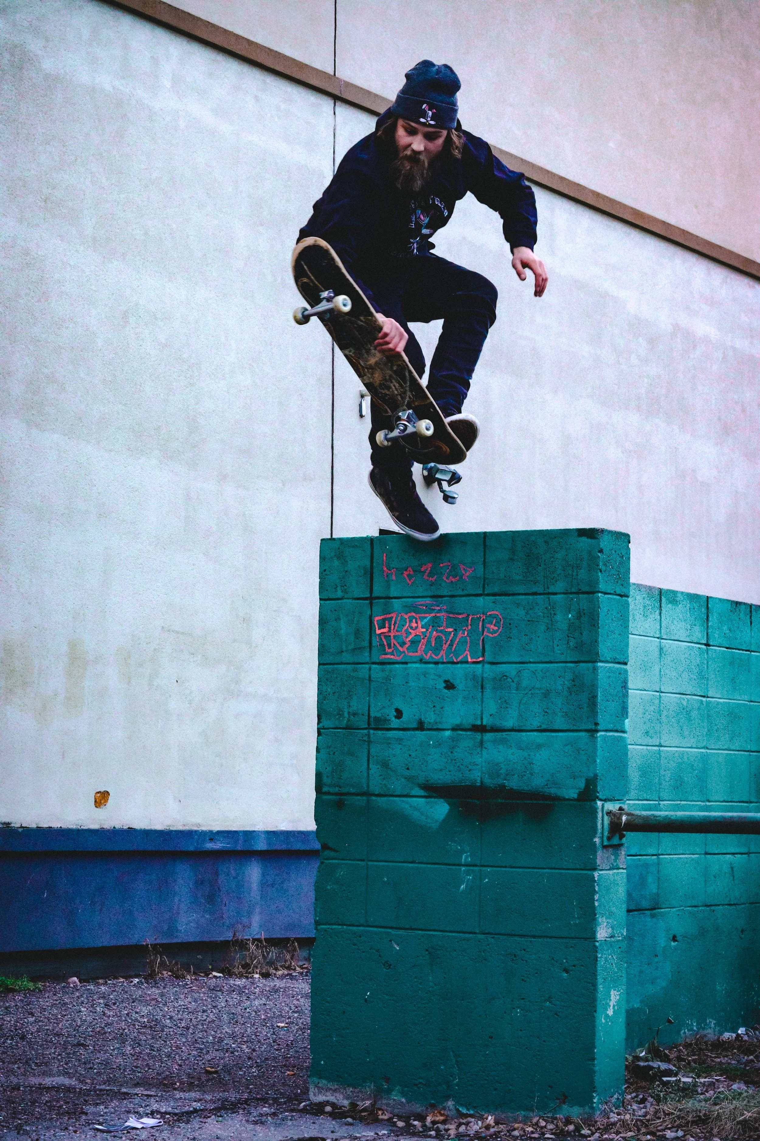Skateboarder performing a jump over a teal brick wall.