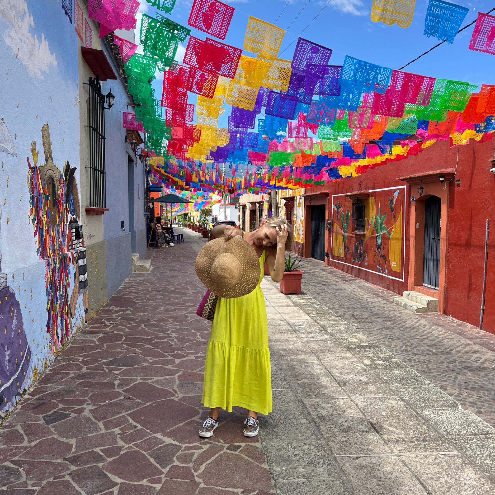 cobblestone street with colorful flags and woman in a yellow dress with a hat in oaxaca city