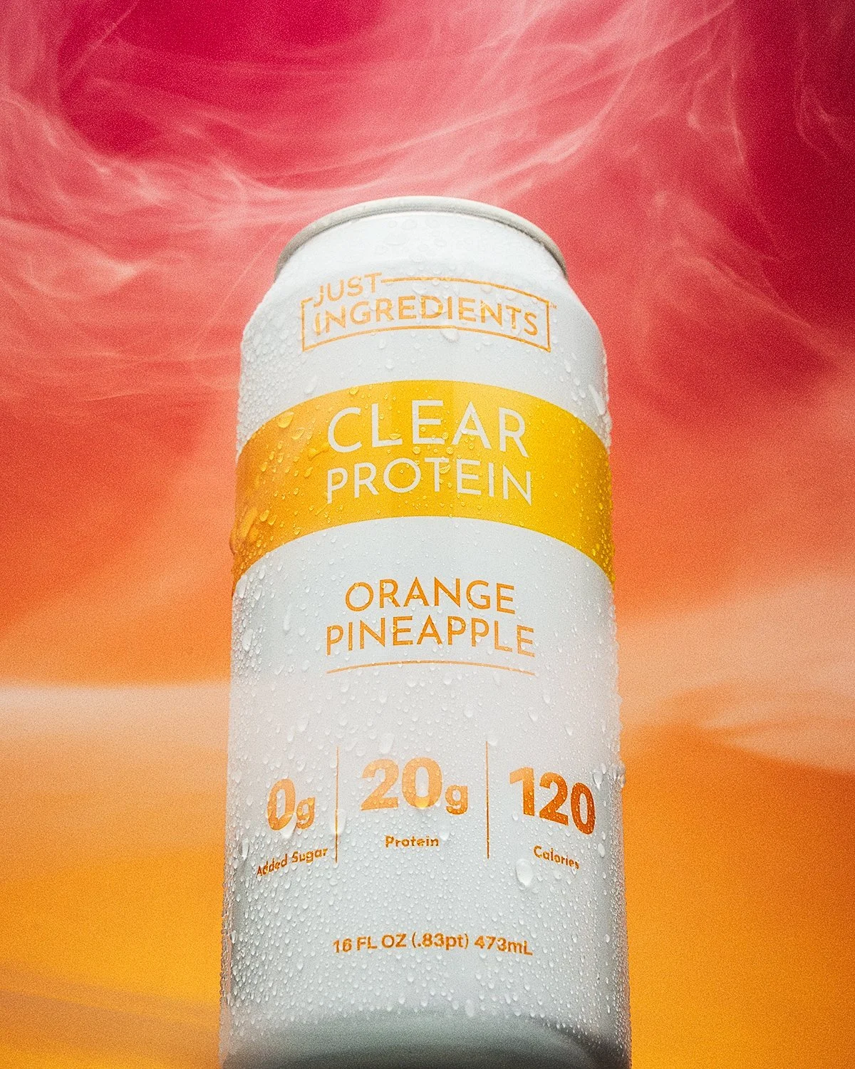 Product photo by NAJ Captured of a Just Ingredients Clear Protein Orange Pineapple can with condensation, framed by smoke against a pink-to-orange backdrop — 20g protein, 0g added sugar, 120 calories