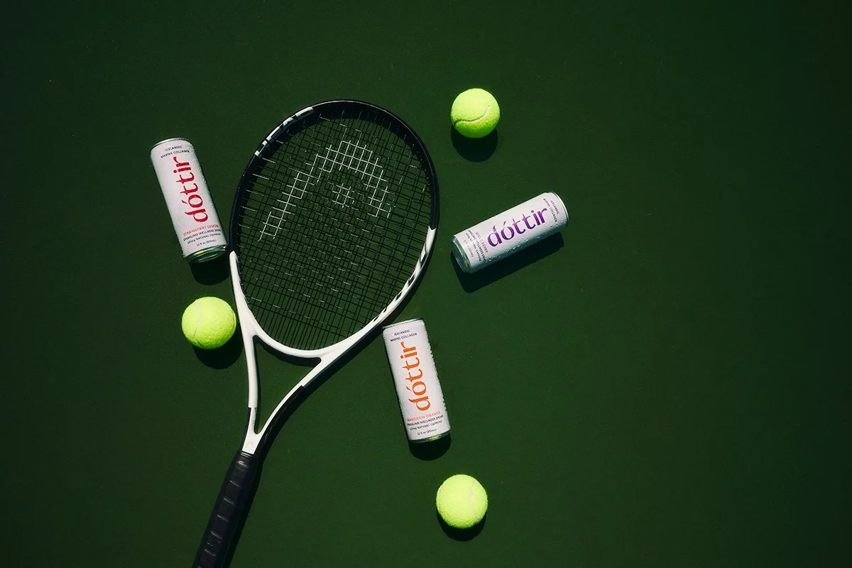 Tennis racket, tennis balls, and Dóttir collagen wellness drinks arranged for a Spring into Summer product photography campaign by NAJ Captured.