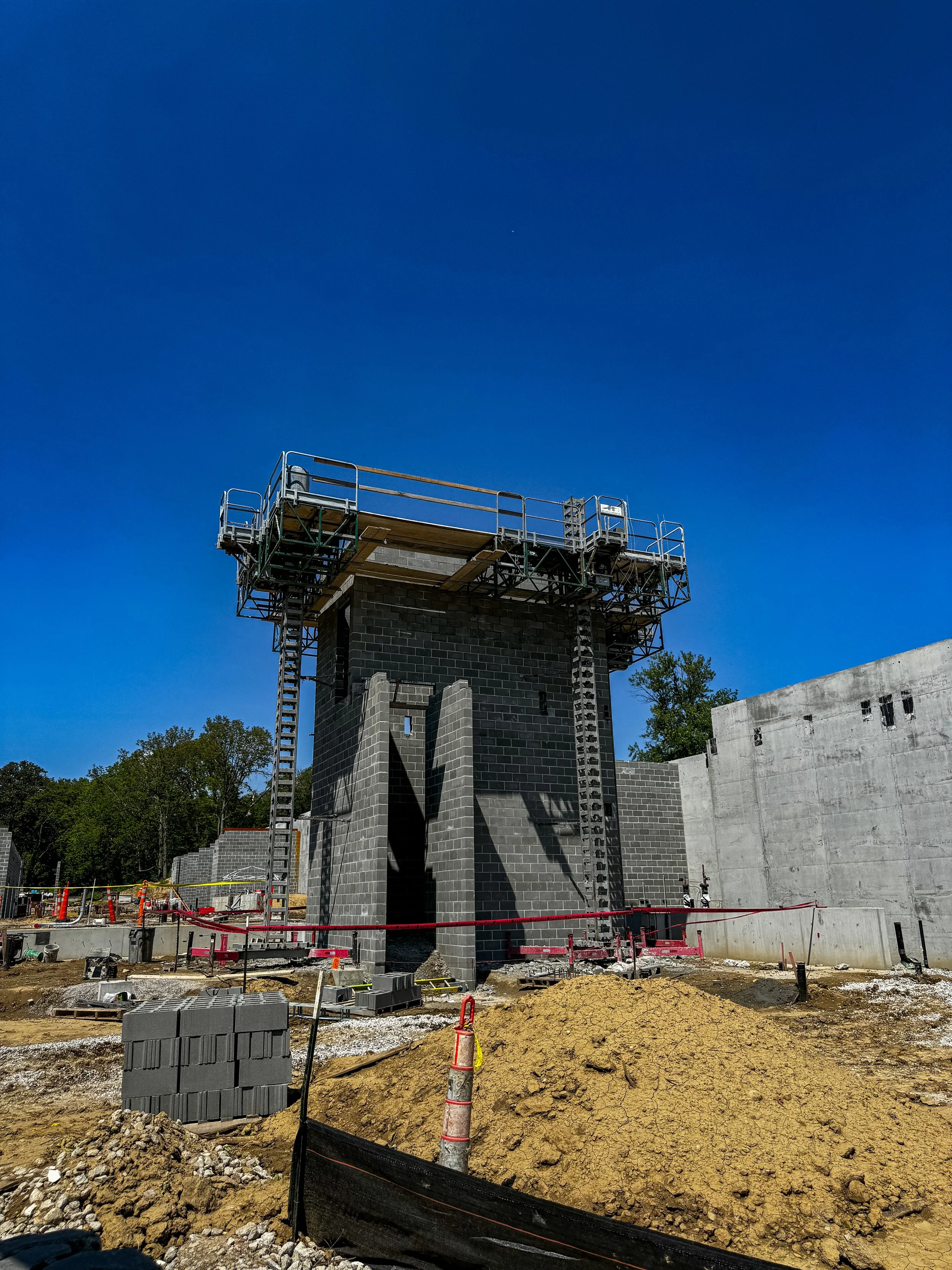 Under construction site with a tall tower and scaffolding, surrounded by dirt and construction materials, with a clear blue sky in the background.