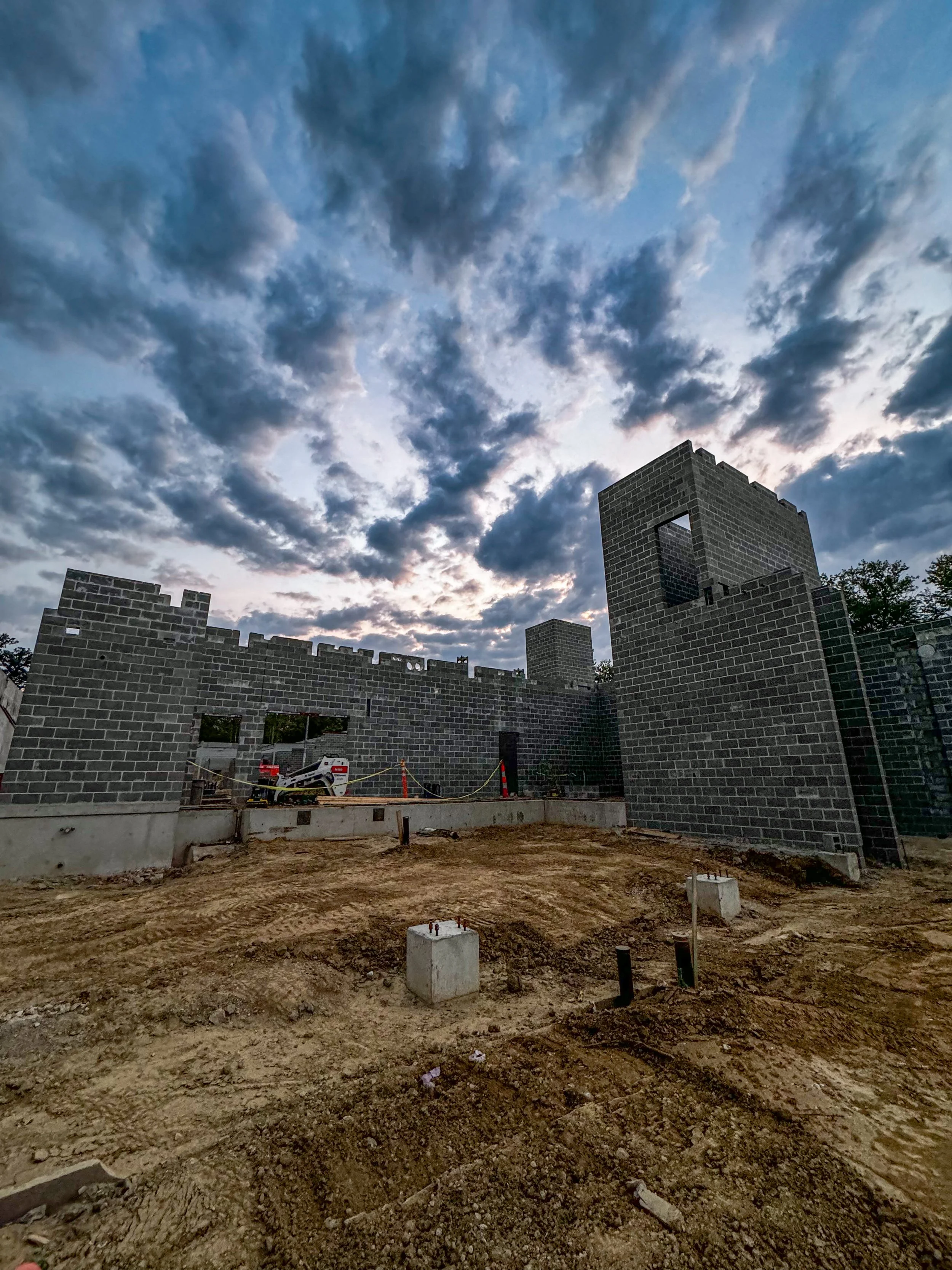 Construction site with unfinished brick walls and a cloudy sky.