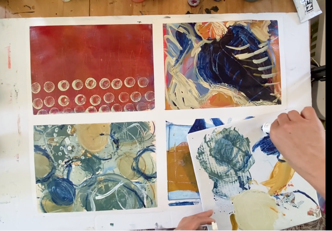 A table with four abstract paintings, including circles, brushstrokes, and swirling patterns in various colors, with someone holding a palette and painting.