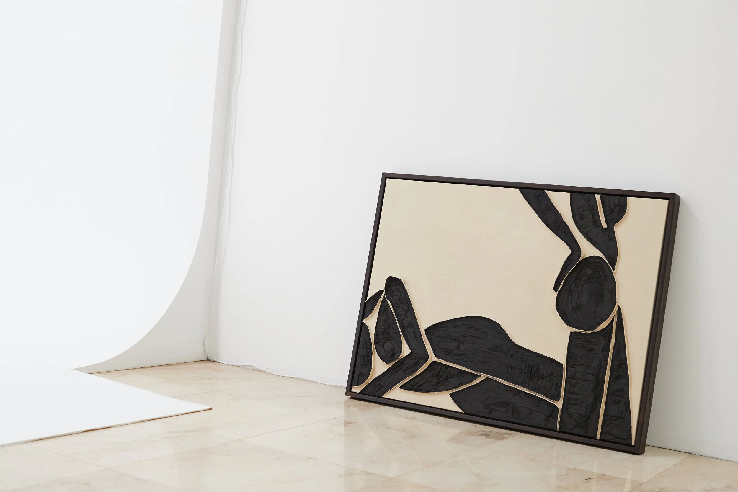 Black textured abstract art piece leaning against a white gallery wall