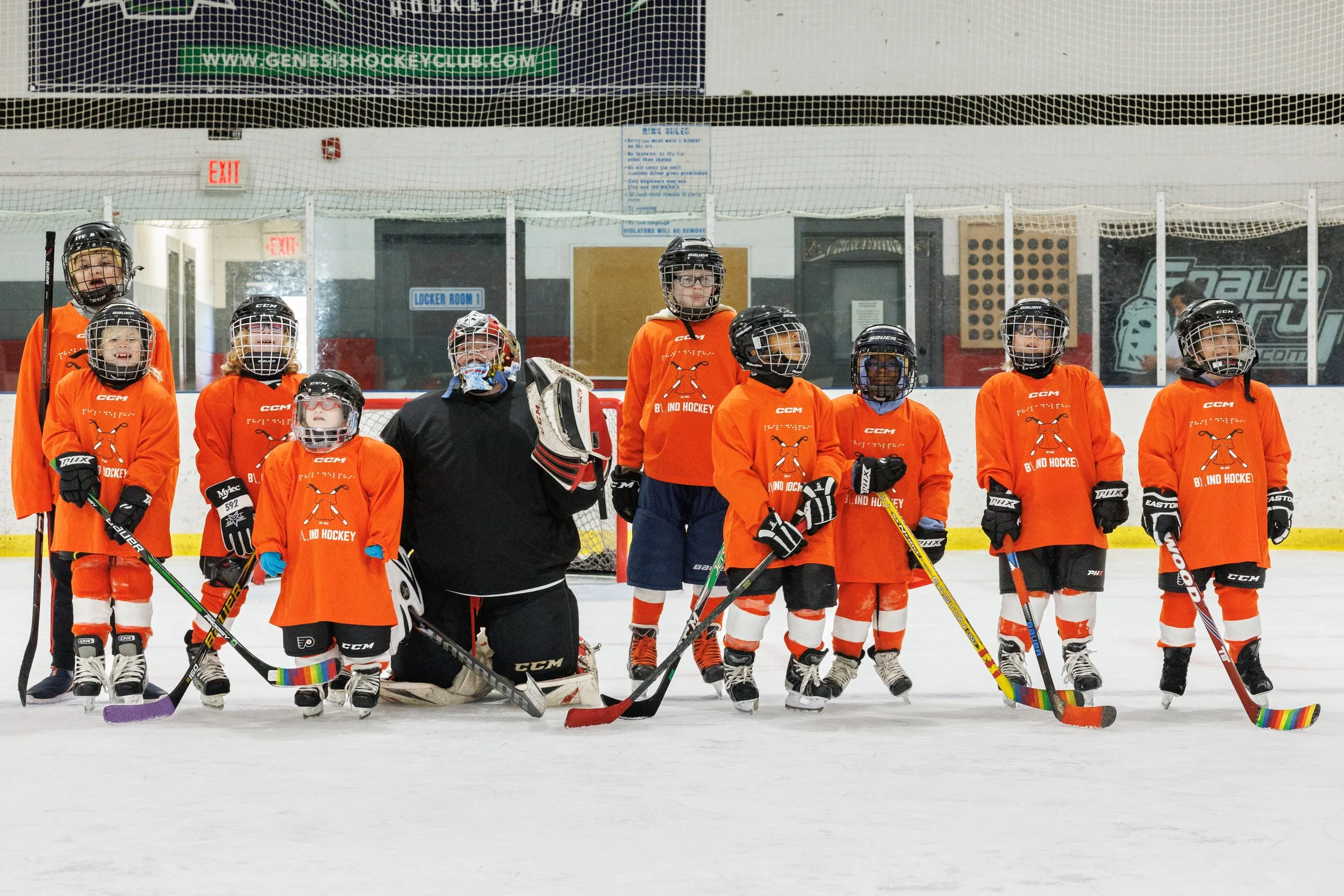 Blind hockey players stand on the ice in orange jerseys