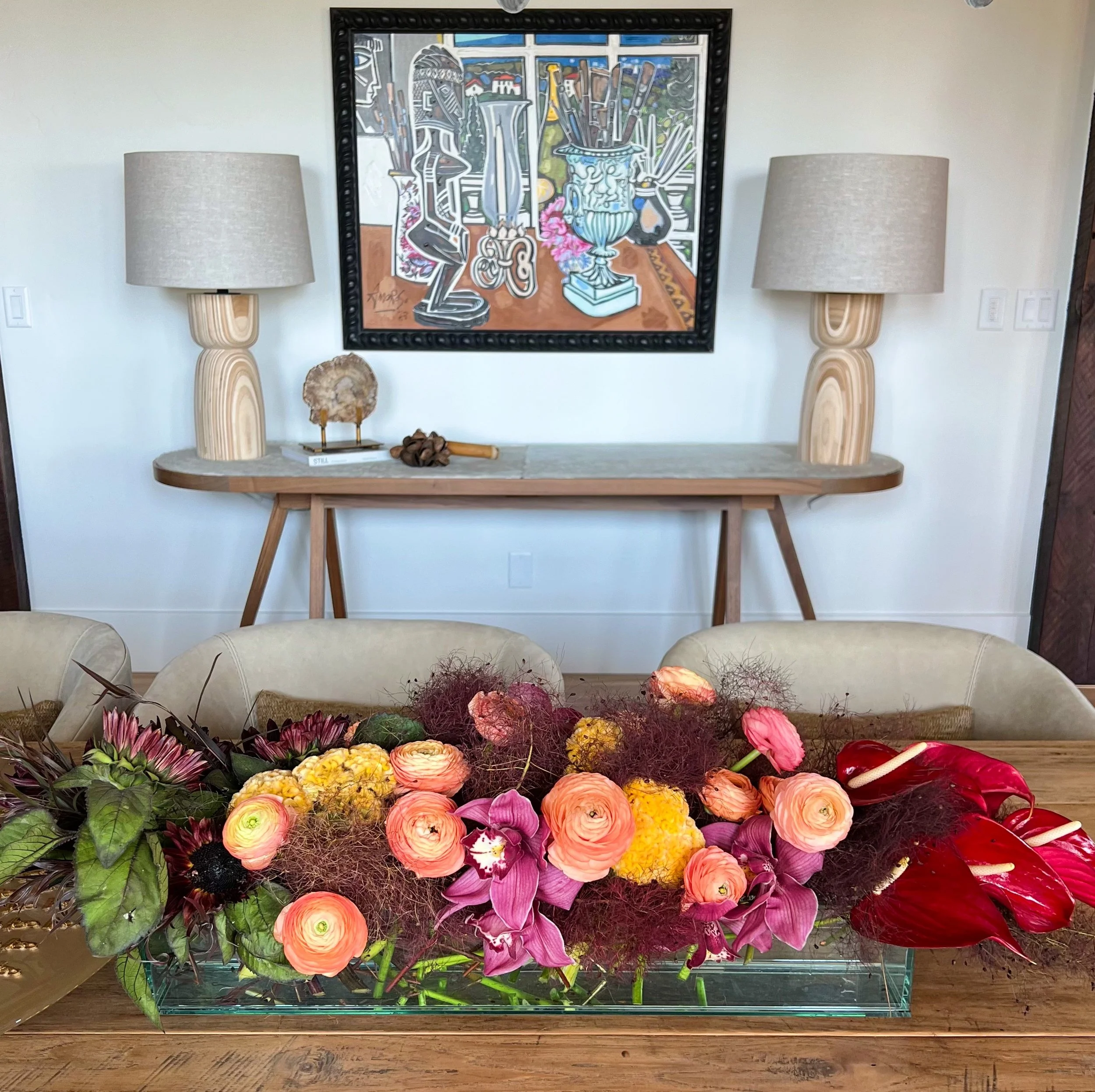 Elegant interior with colorful flower arrangement, wall art, and decorative table with lamps.