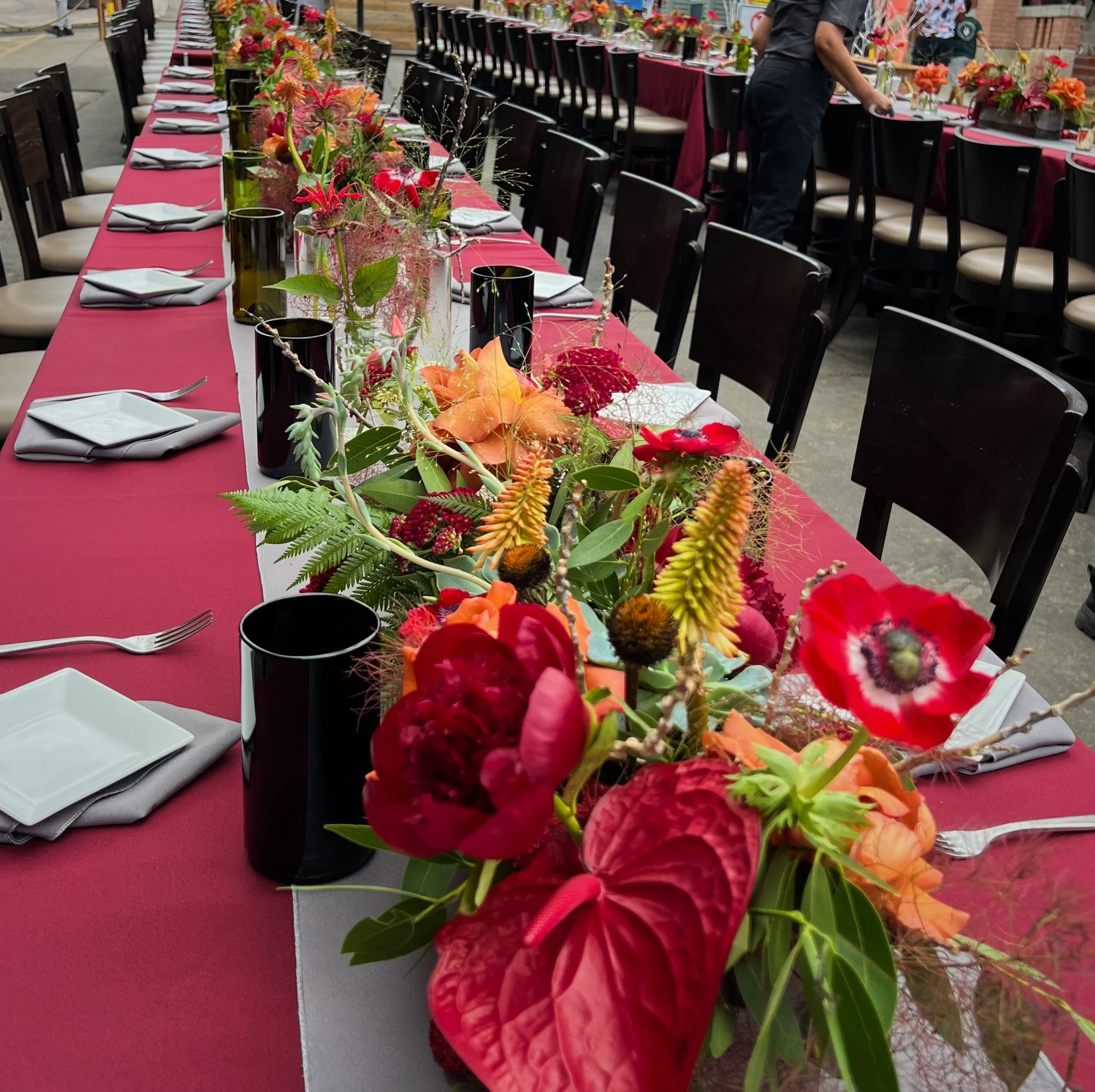 Long dining table decorated with red tablecloth, floral centerpieces, plates, and cutlery arranged for an event.