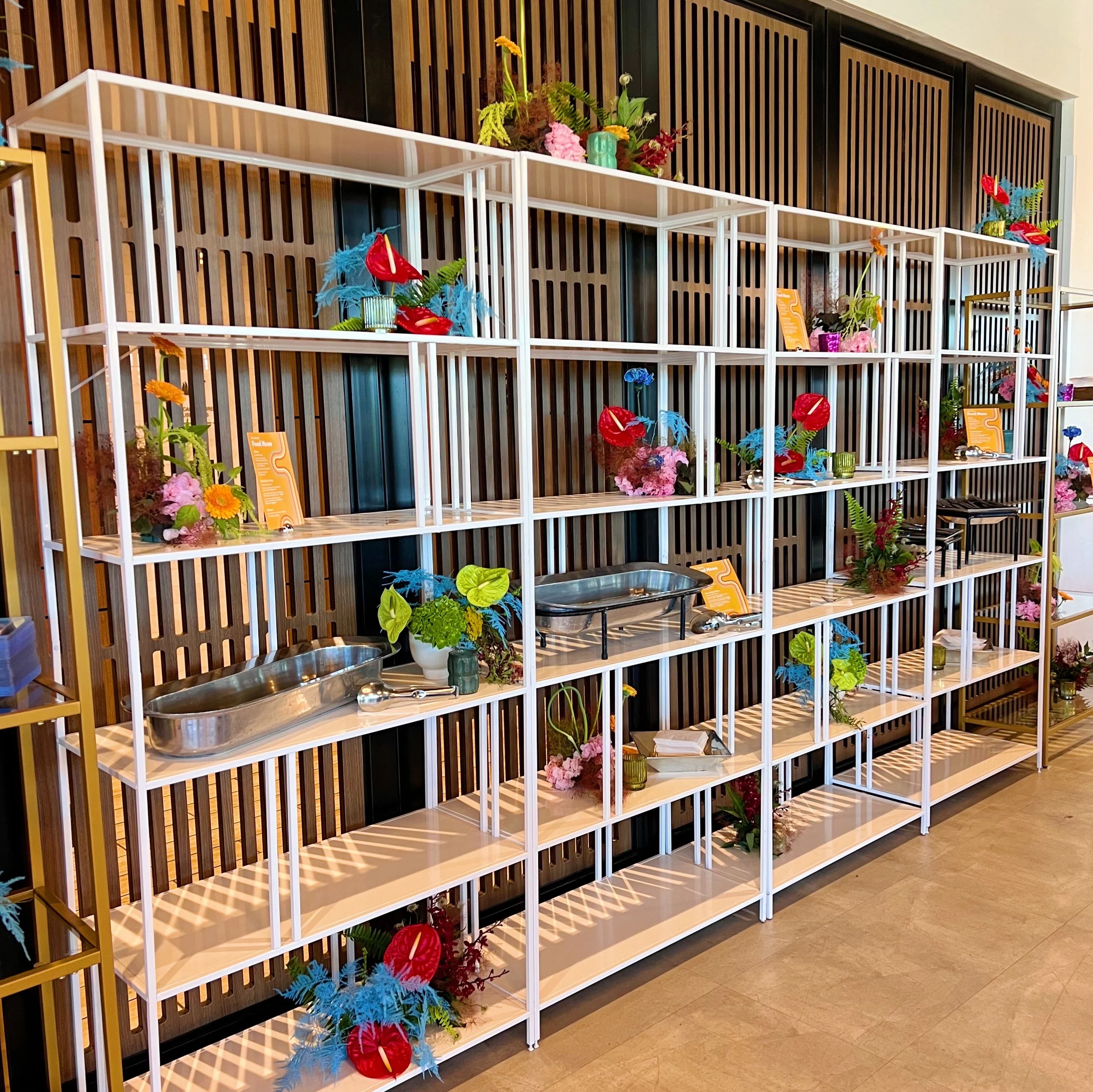 Display shelves with colorful floral arrangements, decorative objects, and some display signs in a modern interior setting.