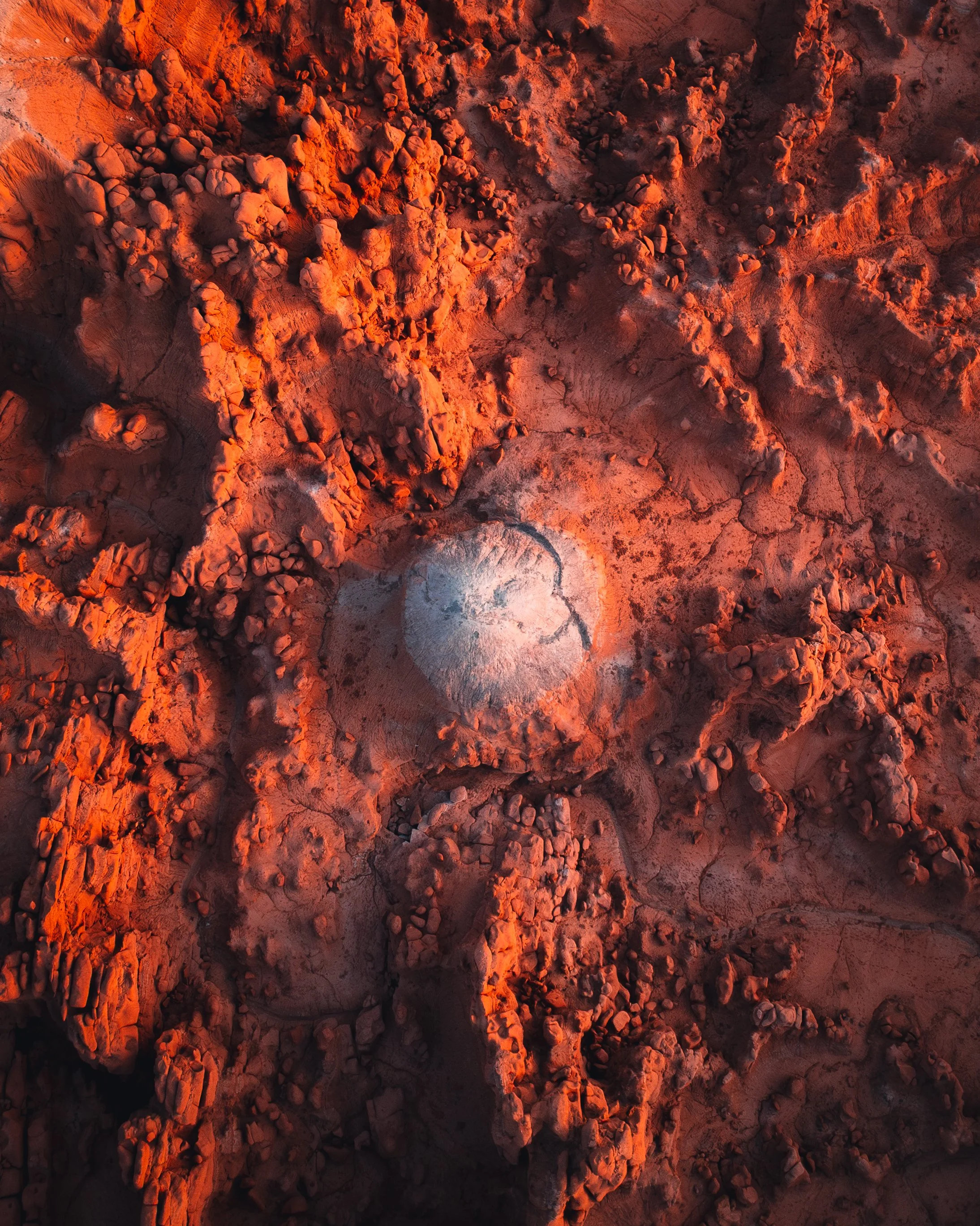 An aerial view of the Martian surface showing red rocks and a large circular impact crater.