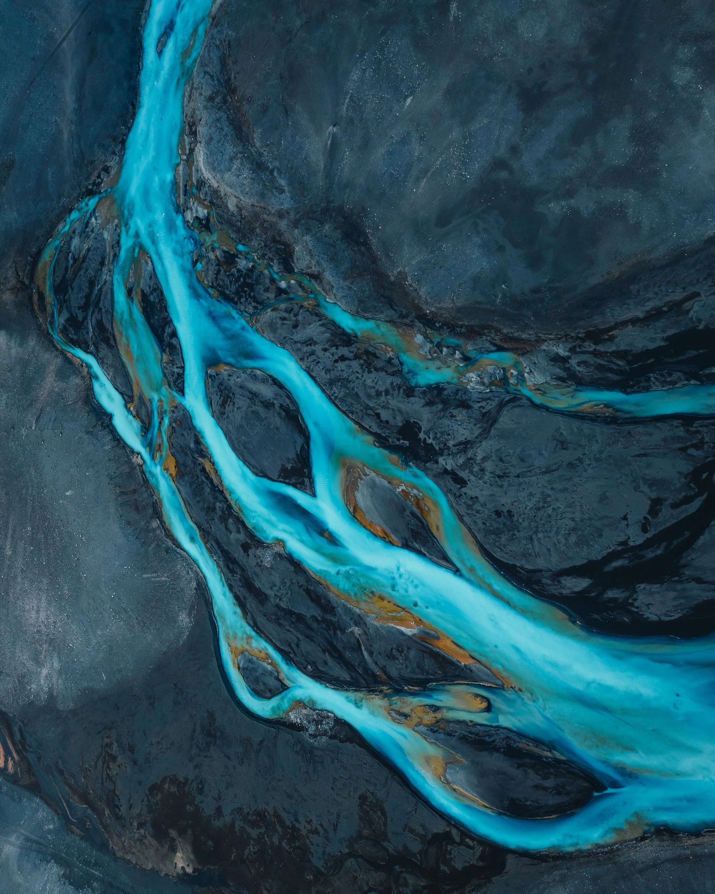 An aerial view of a winding river with bright blue water flowing through a dark, rocky landscape.