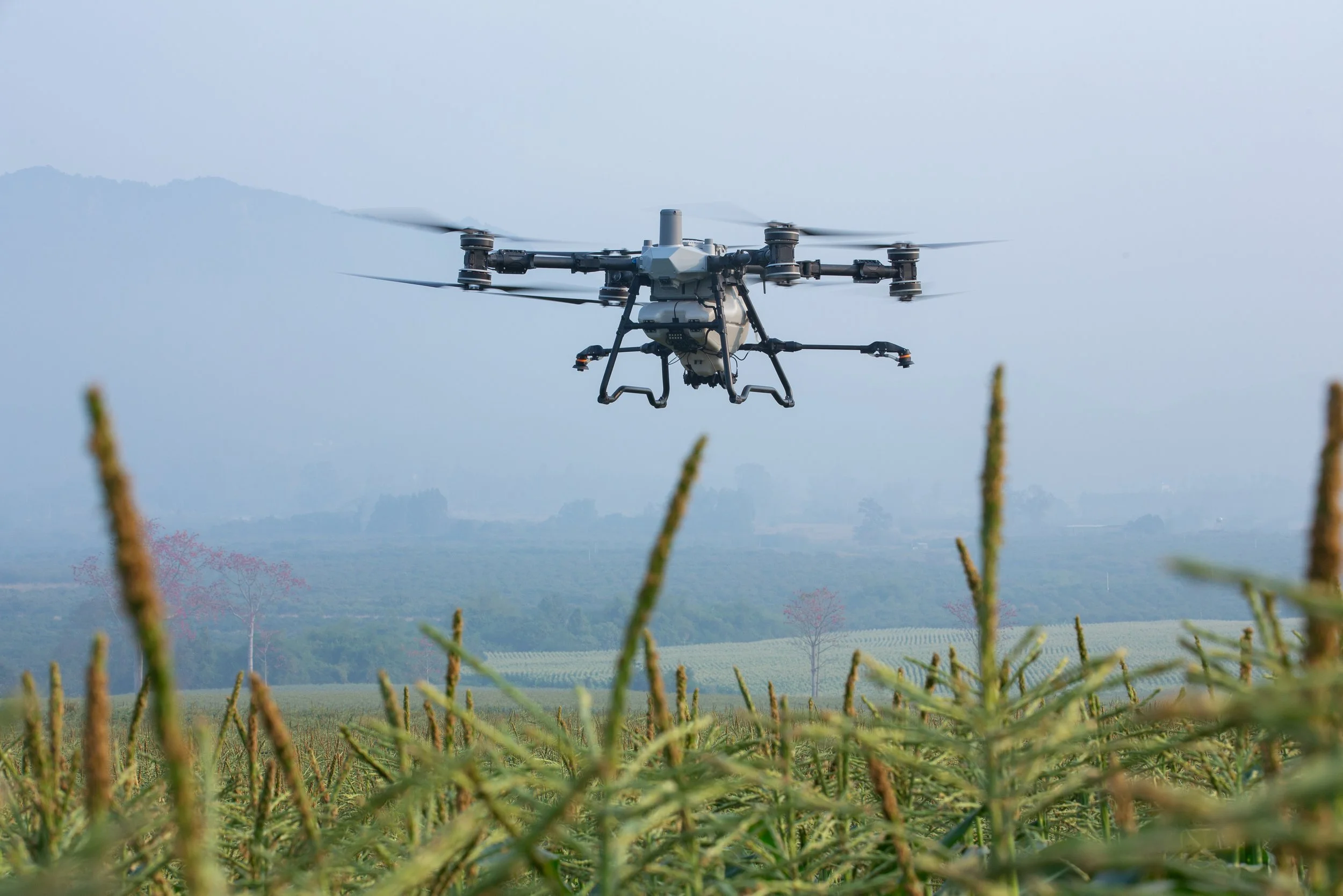 A drone flying over a farm field during daytime with mountains in the background.