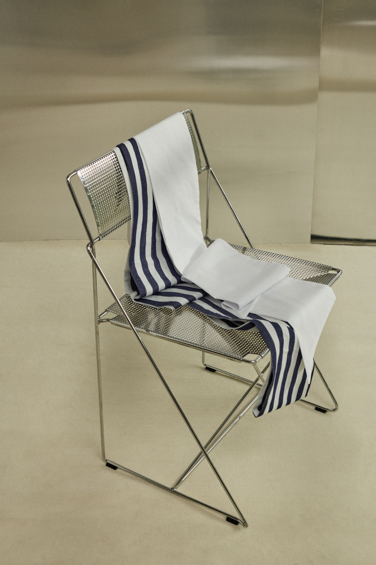 A metal chair with a black and white striped and white cloth draped over it, sitting on a beige floor against a metallic wall.