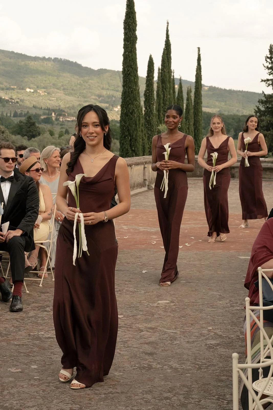 Bridesmaids in elegant burgundy dresses carrying single-stem calla lilies at a romantic destination wedding at Villa Medicea di Lilliano in Florence, Italy.