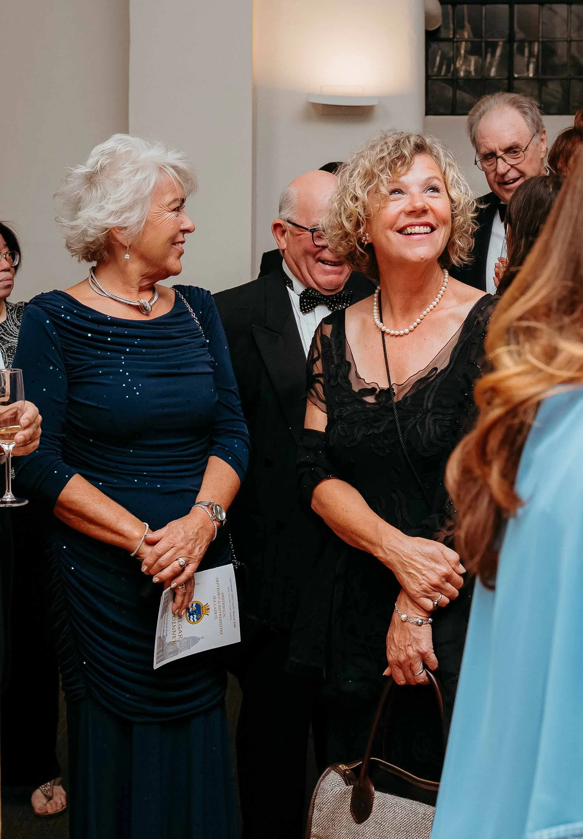 A group of elderly people dressed in formal attire at a social event, smiling and engaging with each other.