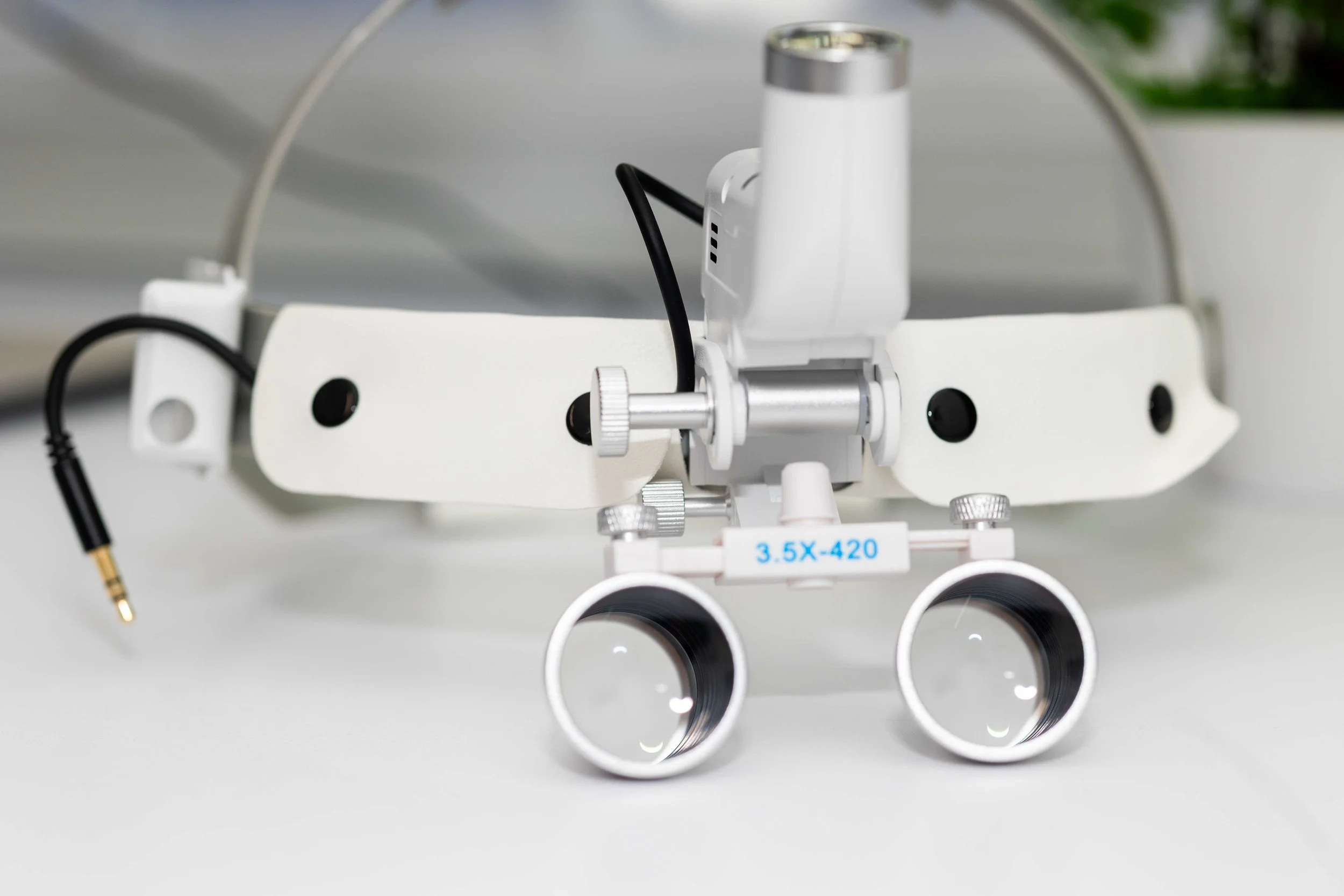 Close-up of a white medical or scientific device with lenses, screws, and cables on a white surface.