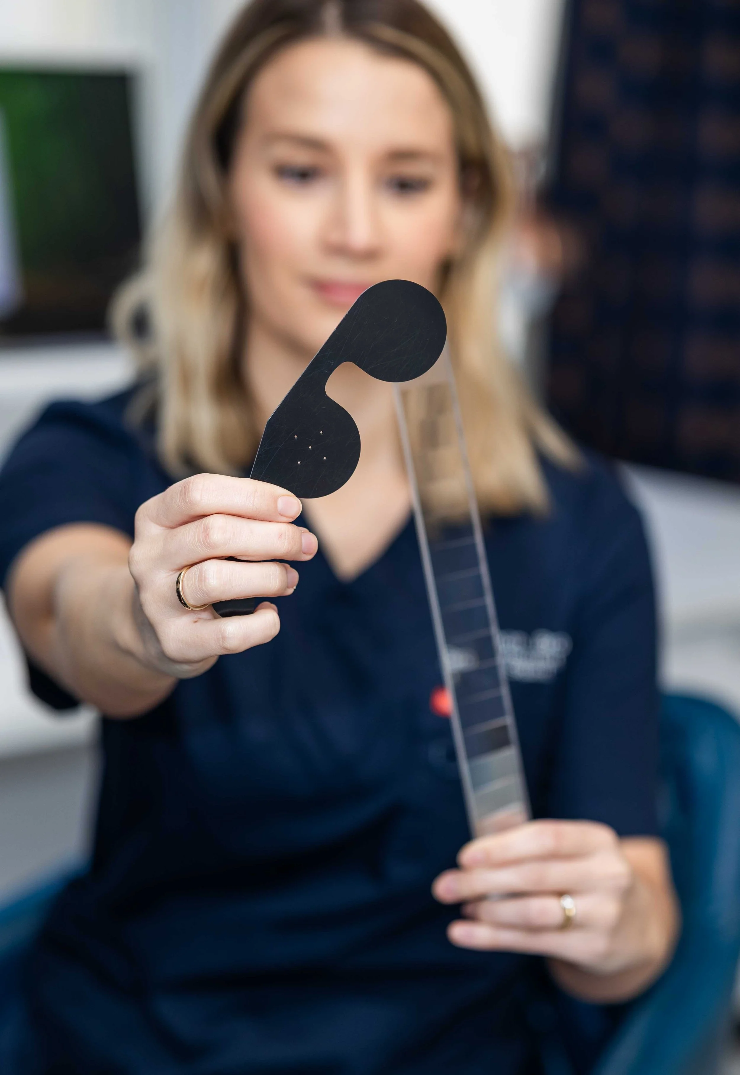 A woman holding a pain relief patch and a thin, transparent ruler in an office setting.