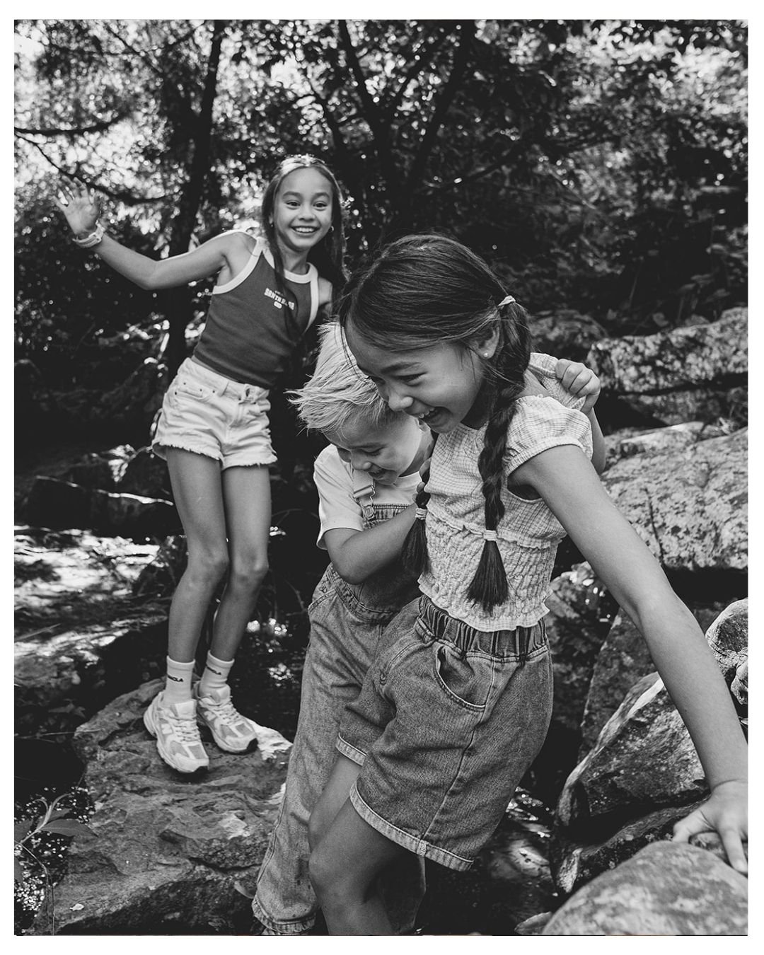 Candid family photoshoot in Greenwich Park. Portrait of siblings playing on rocks.