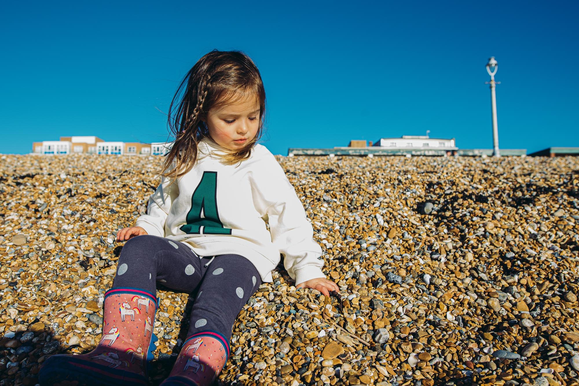 family-portrait-girl-playing-beach-pebbles-blue-sky-family-photographer-brighton-hove-worthing-lewes.jpg