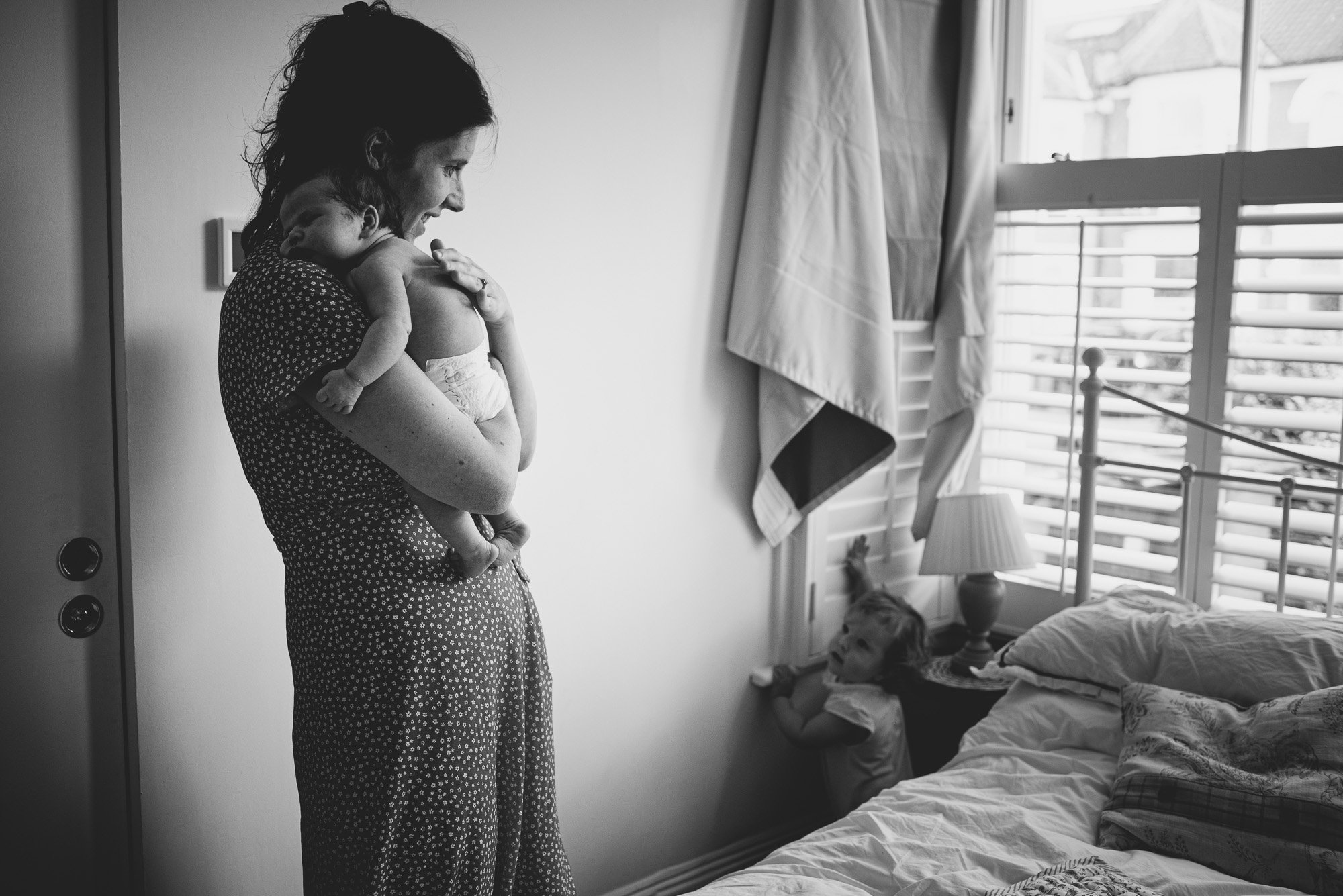 unposed-family-photoshoot-newborn-baby-in-arms-mum-toddler-near-window-at-home-family-photoshoot-brgihton-london.jpg