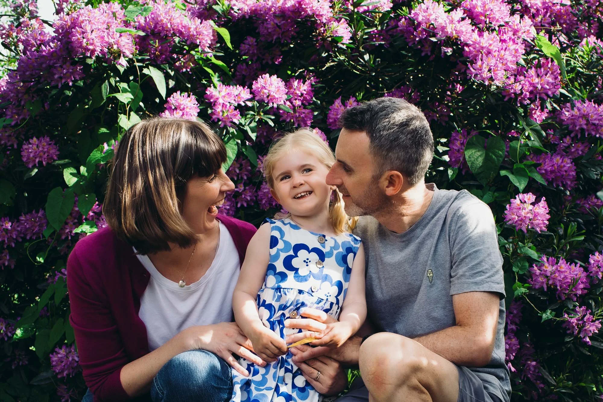 Uckfield family photoshoot in a local park. Natural family lifestyle photography in Uckfield, Horsham, Haywards Heath and across Sussex. Portrait of parents and their daughter with flowers.