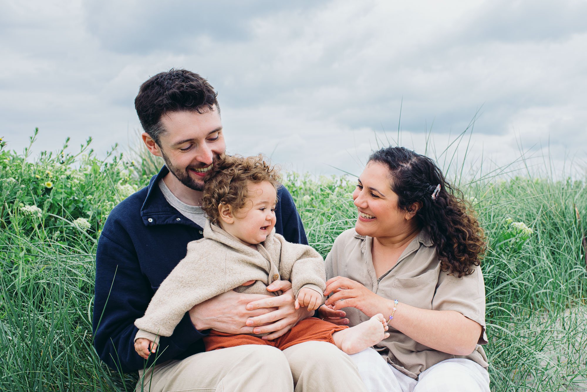 family-portrait-session-west-wittering-beach-girl-on-lap-sitting-in-sand-clouds-in-sky-sussex-family-photographer.jpg