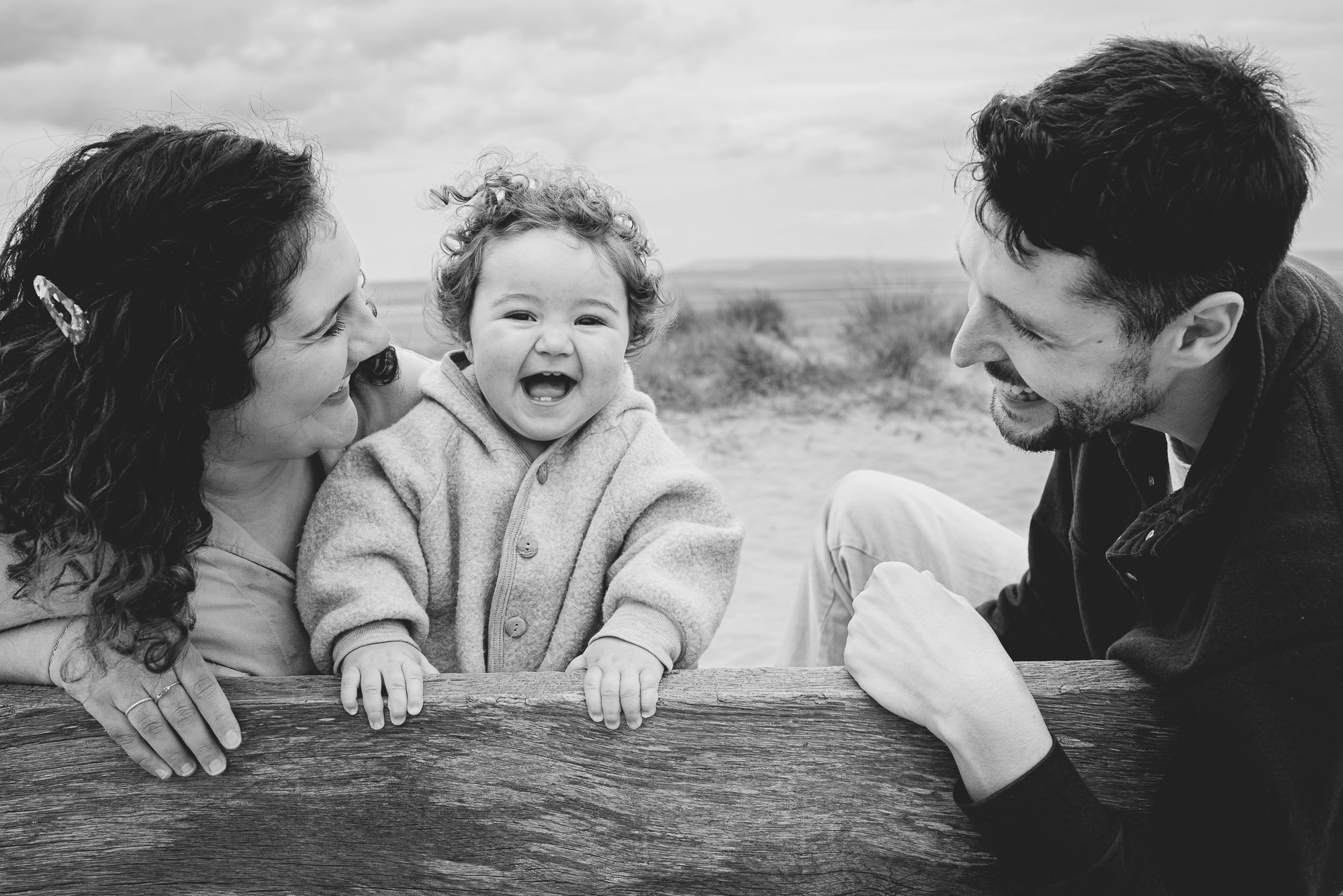 parents-toddler-portrait-laughing-sitting-on-bench-in-sand-west-wittering-beach-west-sussex-family-photography.jpg