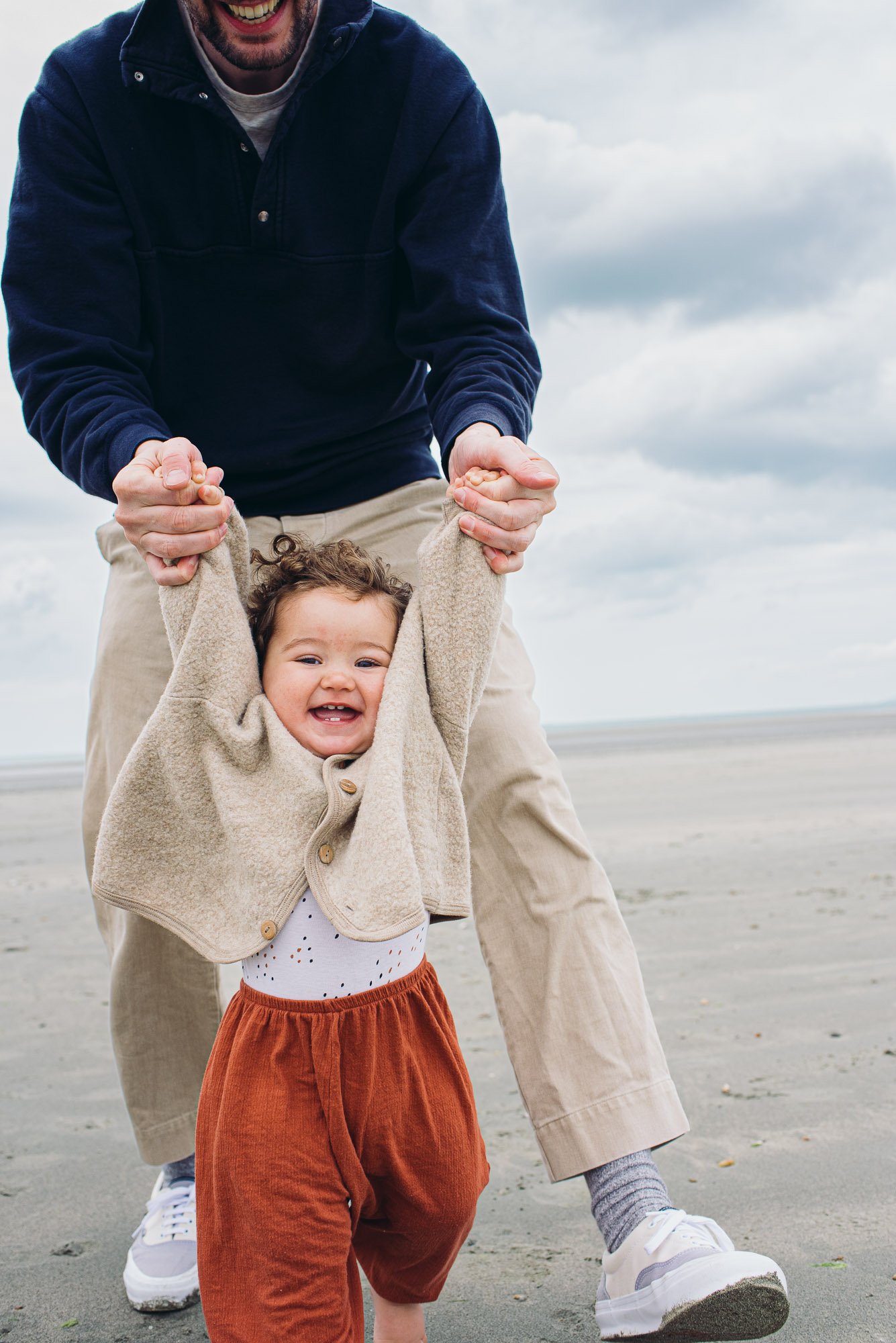 girl-swinging-daddies-hands-beach-sand-sea-clouds-chichester-professional-family-photographer.jpg