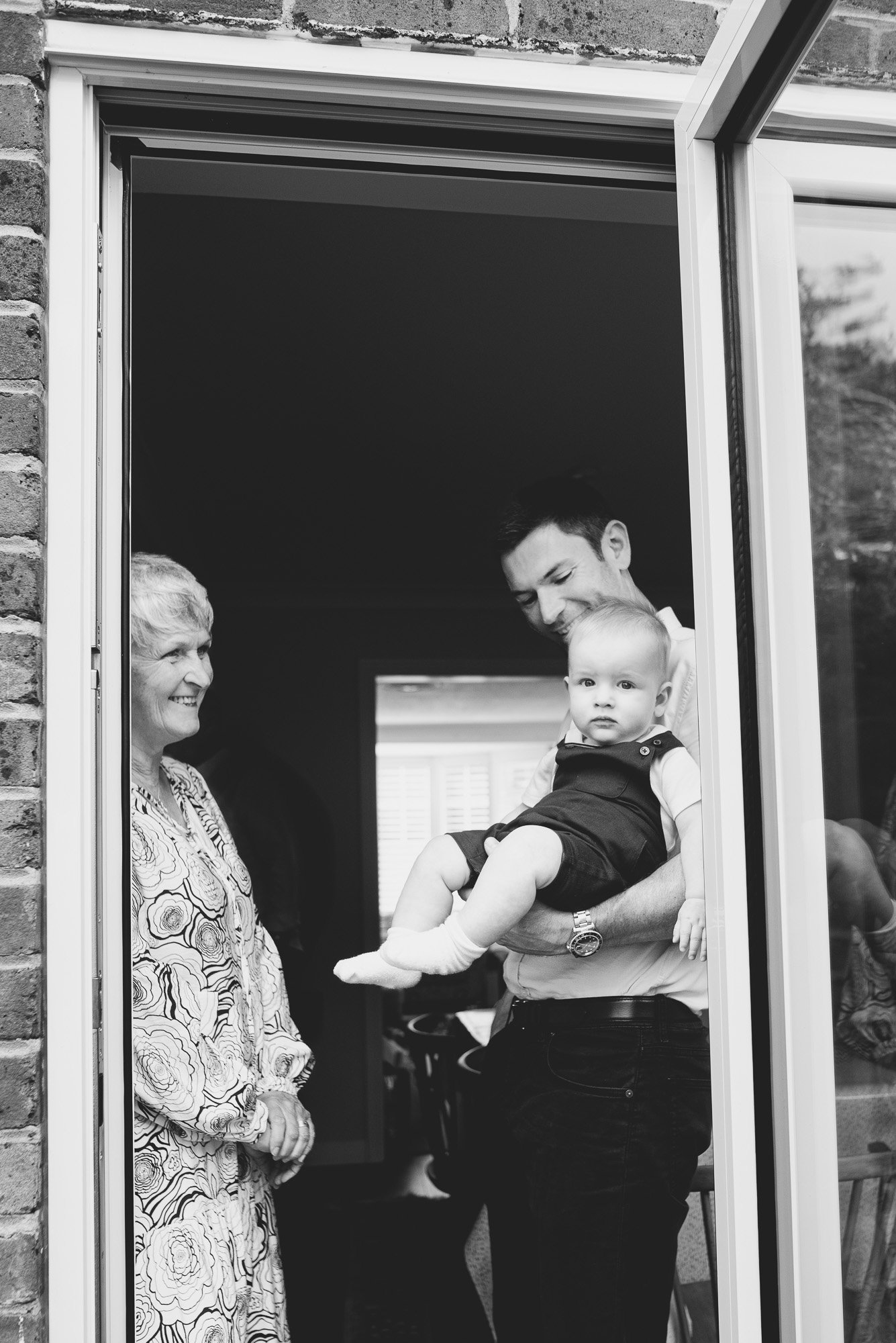 dad-baby-boy-at-home-with-aunt-family-photoshoot-before-christening-starts-natural-black-and-white-children-photography.jpg