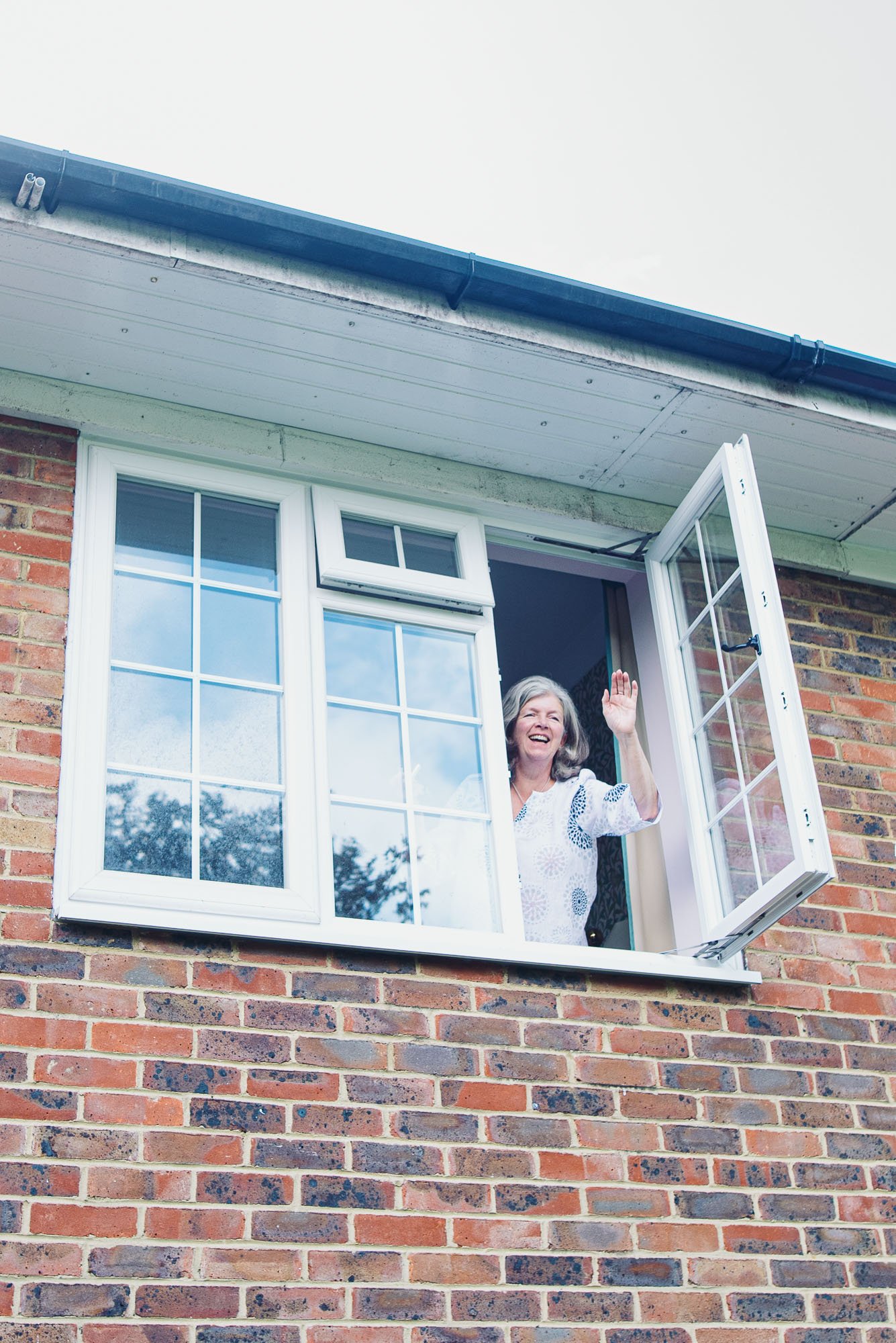gradmother-waving-bedroom-window-during-family-documentary-photoshoot-at-home-hove-sussex.jpg
