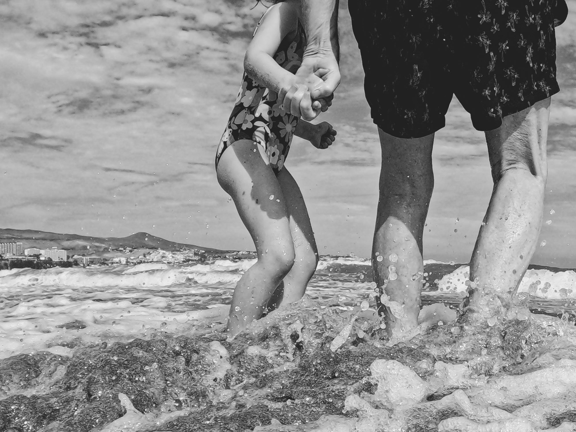 family-photo-shoot-beach-natural-unposed-grandfather-granddaughter-holding-hands-in-sea-black-and-white-art-photographer.jpg