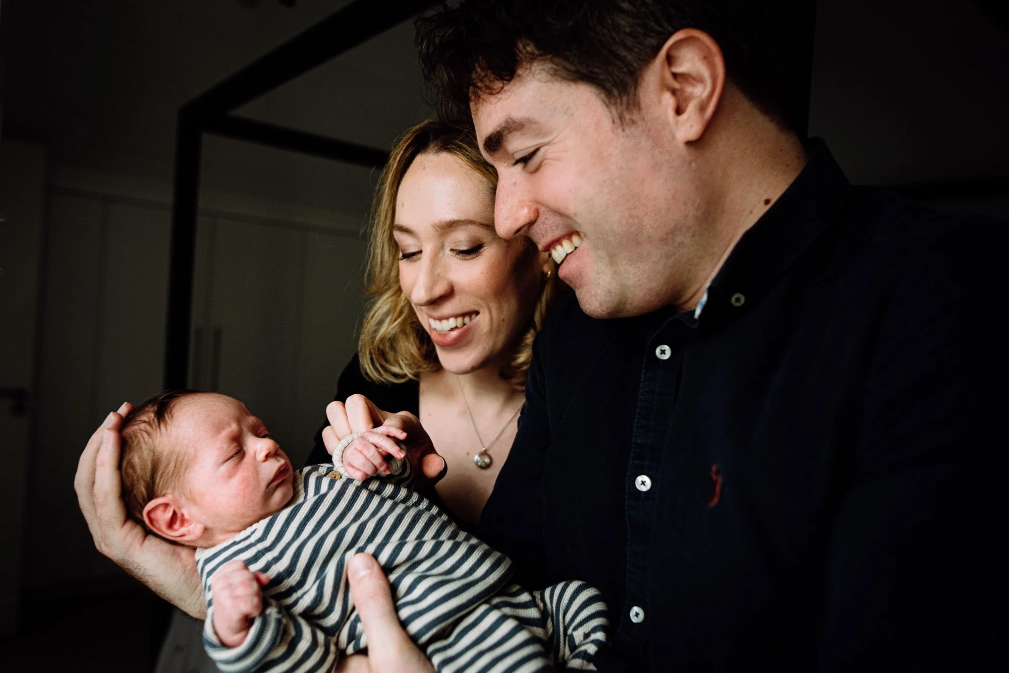 Teddington newborn photographer offering in-home newborn sessions in South West London. New parents looking at their newborn baby boy, smiling.