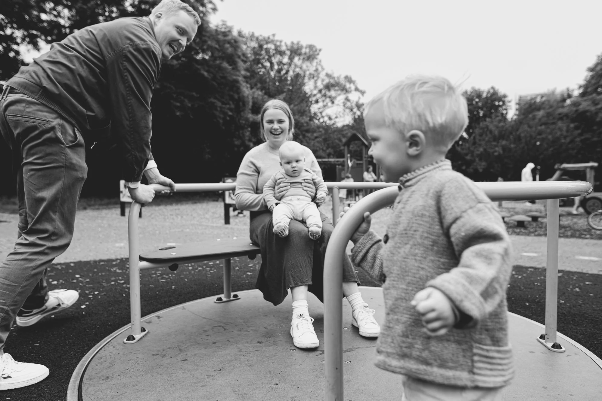 Unposed family portrait taken at a Sussex playground. Baby brother on mother's lap, big brother pushing, and dad.