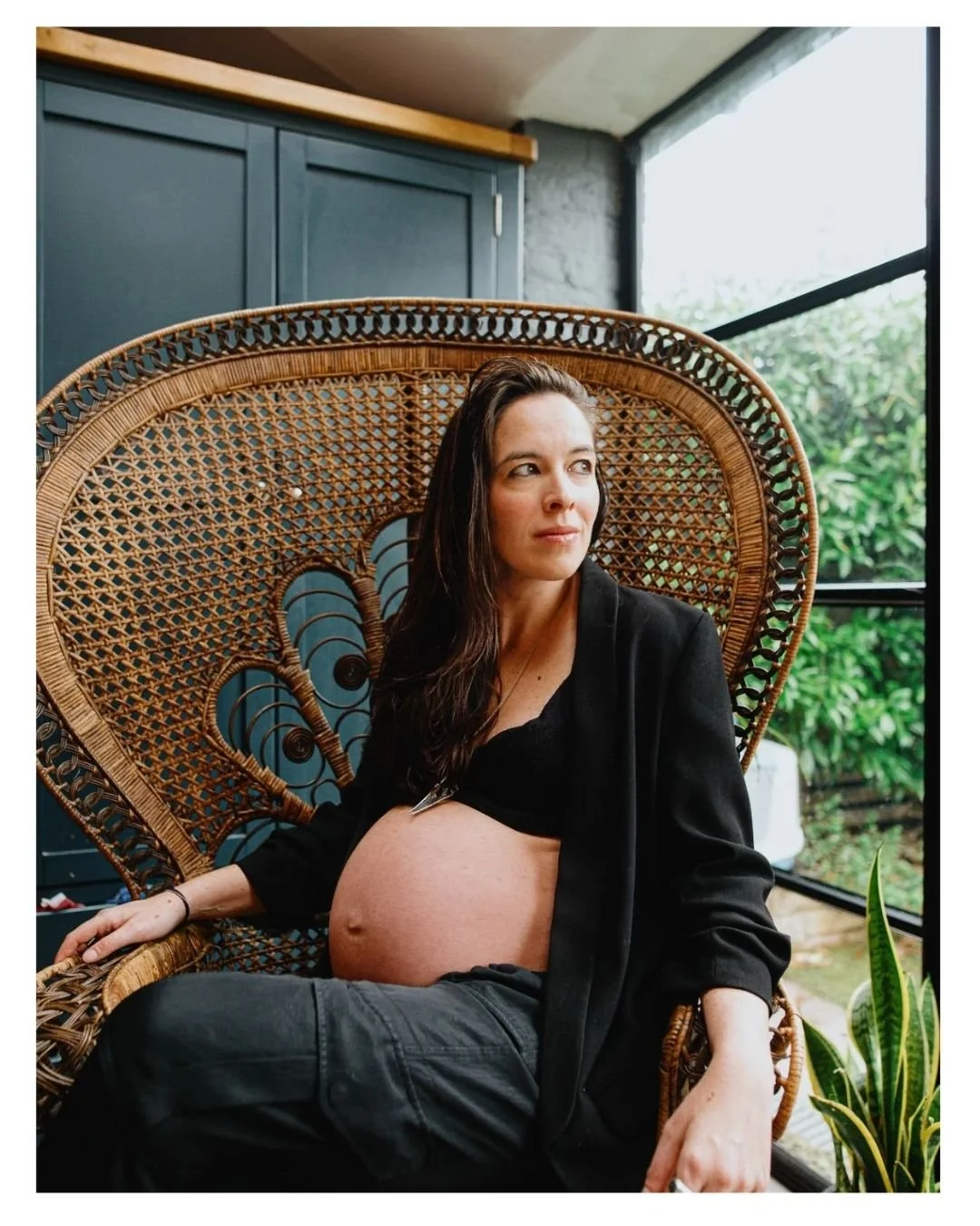 At home maternity photoshoot in Worthing, West Sussex. Pregnant woman in chair looking out of window.