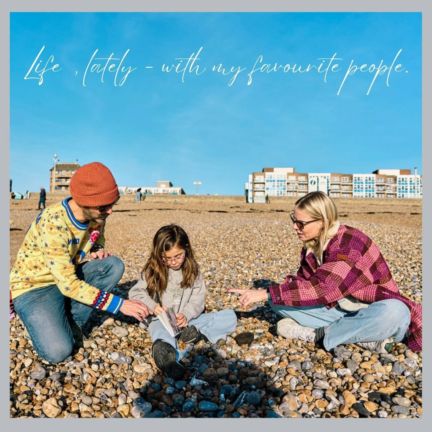 Beach family photoshoot at Hove seafront, Sussex family photographer during her own family photo session in Brighton and Hove. Sitting on the pebbles, blue sky, winter sun, unposed family photos.