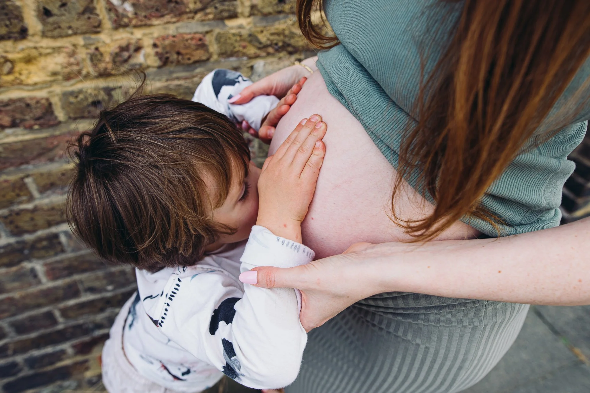 Worthing natural maternity photography, older sibling kissing pregnant belly of mother.