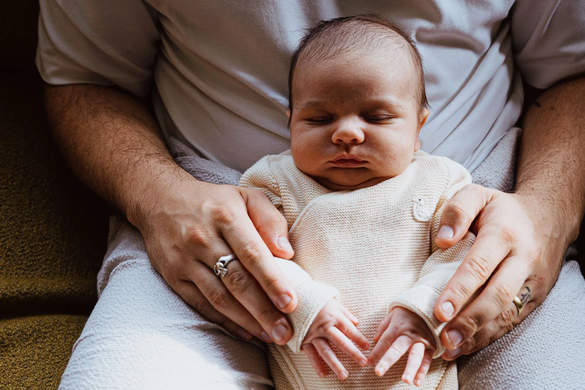 Surrey newborn photographer capturing newborn baby boy asleep on dad's lap. In-home newborn photoshoot in Esher.