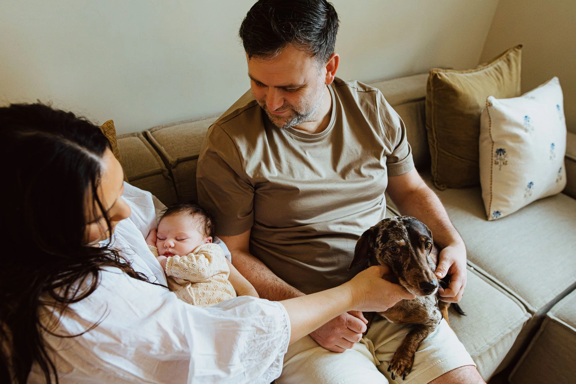 Natural family portrait of new parents, newborn baby, dog, taken at home on the sofa in Portslade, Brighton and Hove.