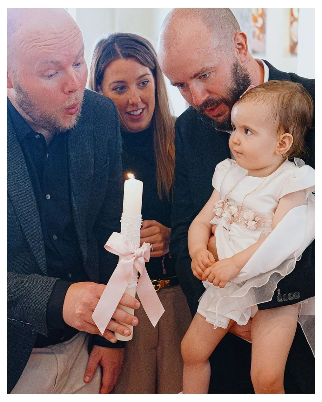 Godfather blowing out candle during girl'ss christening ceremony in church in Chelsea, London. reportage style christening photography in Chelsea and across London.