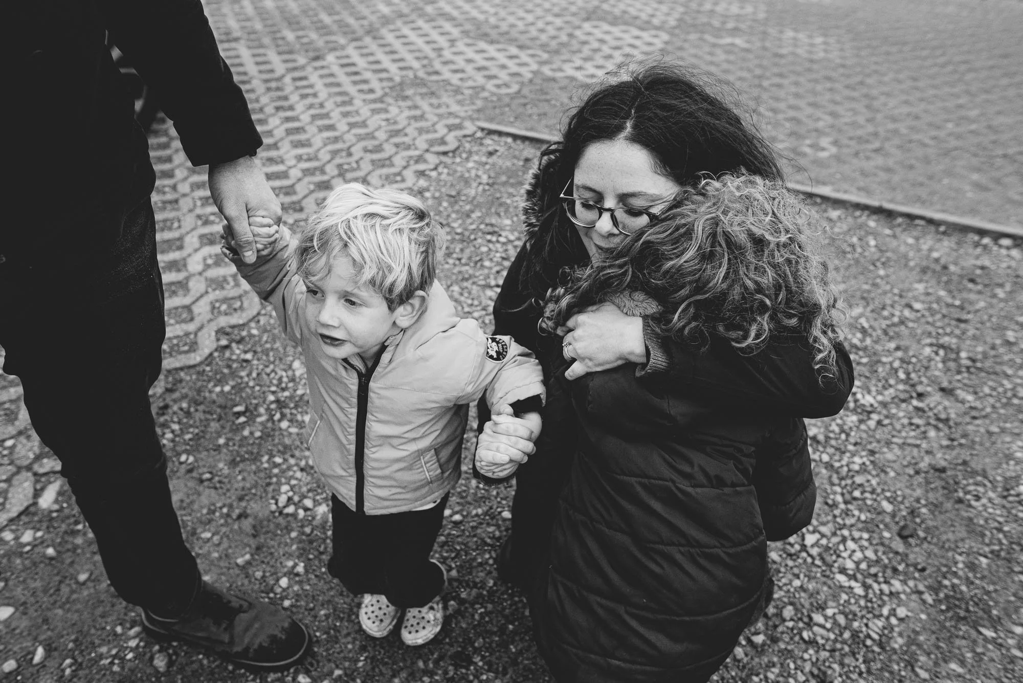 Mother hugging child and holding kid's hand. Black and white natural family portrait photography in East Dulwich, Dulwich Village, Peckham and across South East London.
