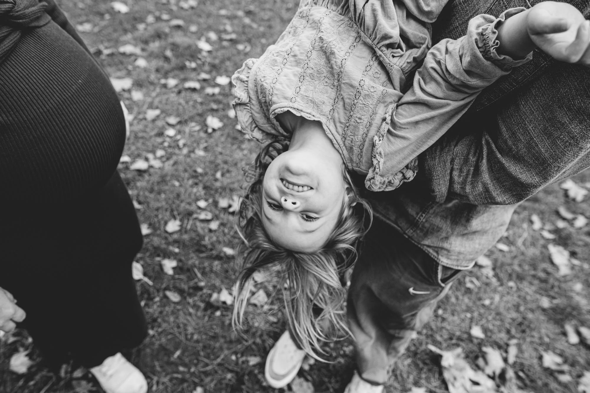 Teddington family photographer capturing girl hanging up side down being held by dad in Bushy Park in Teddington, South West London. Mum pregnant with second child.