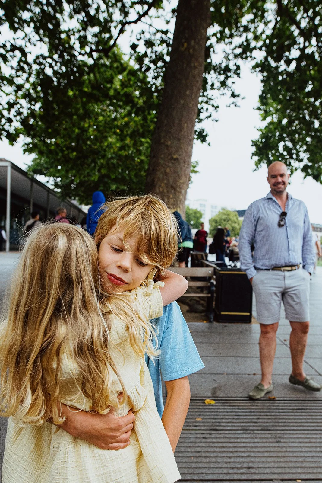 Siblings hugging, dad smiling in background. Unposed London family photoshoot with professional family photographer Irma Arrowsmith.