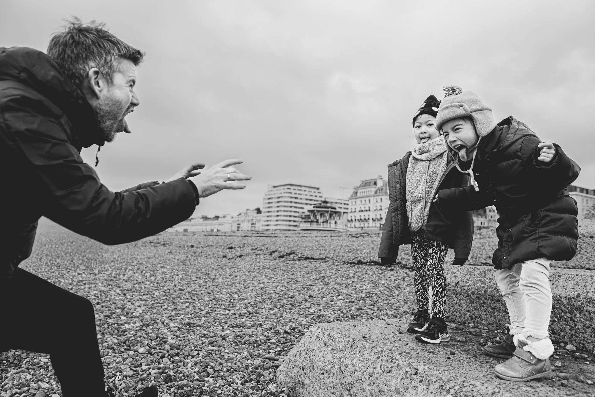 Natural candid portrait of girls and dad taken on Brighton beach on a cold winter day. Unposed candid family photography in Brighton, Hove, Worthing and across Sussex.
