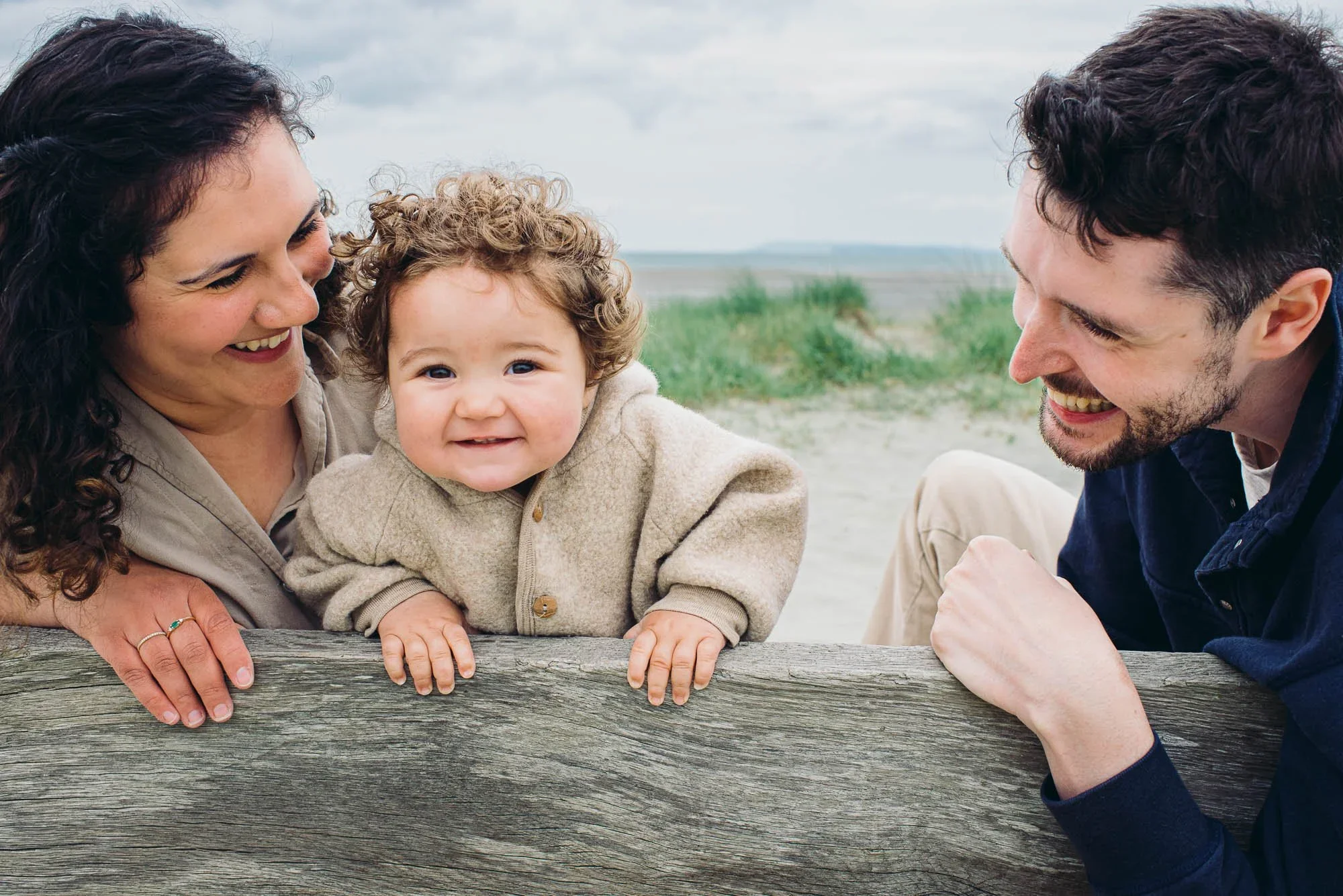 Bosham family photographer capturing natural family portrait of parents and toddler girl at West Wittering Beach, West Sussex on a cloudy Summer day in August.