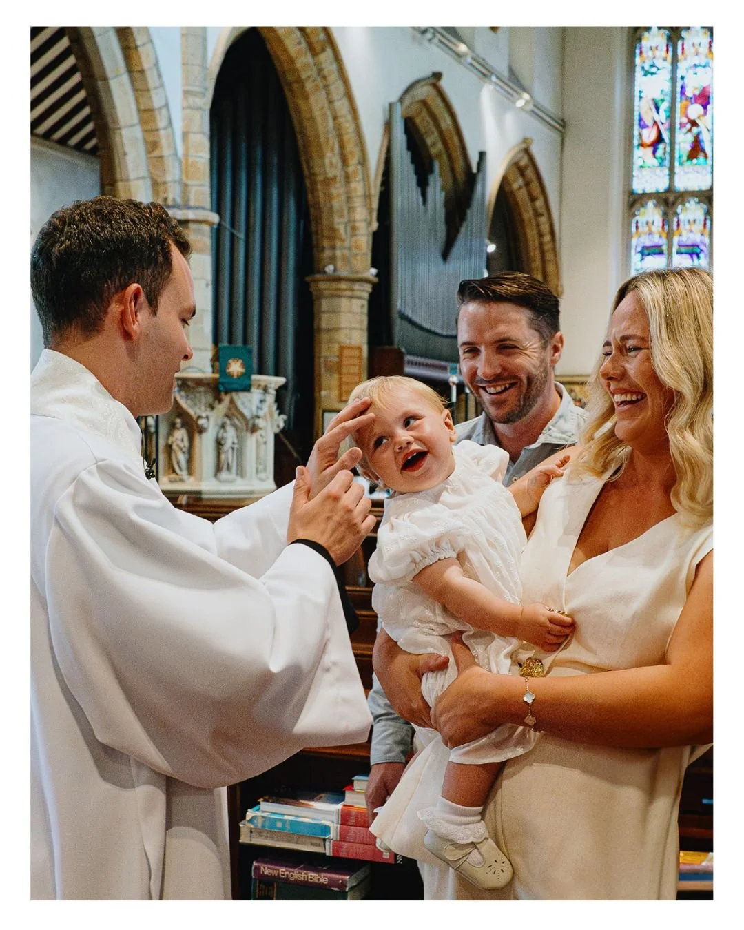 London Christening photographer documentary style, priest blessing baby girl in London church.