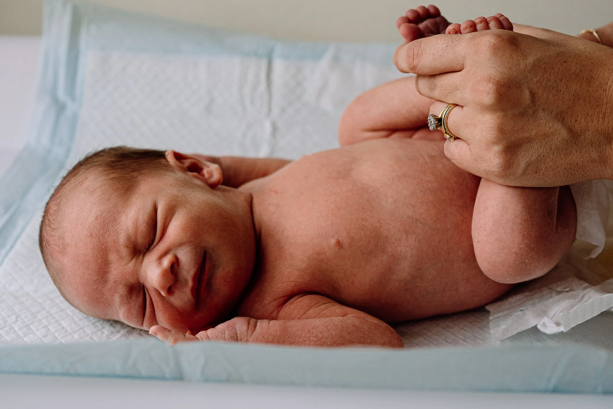 Guildford newborn photographer capturing baby boy getting changed by his mother during natural in-home newborn baby photoshoot.