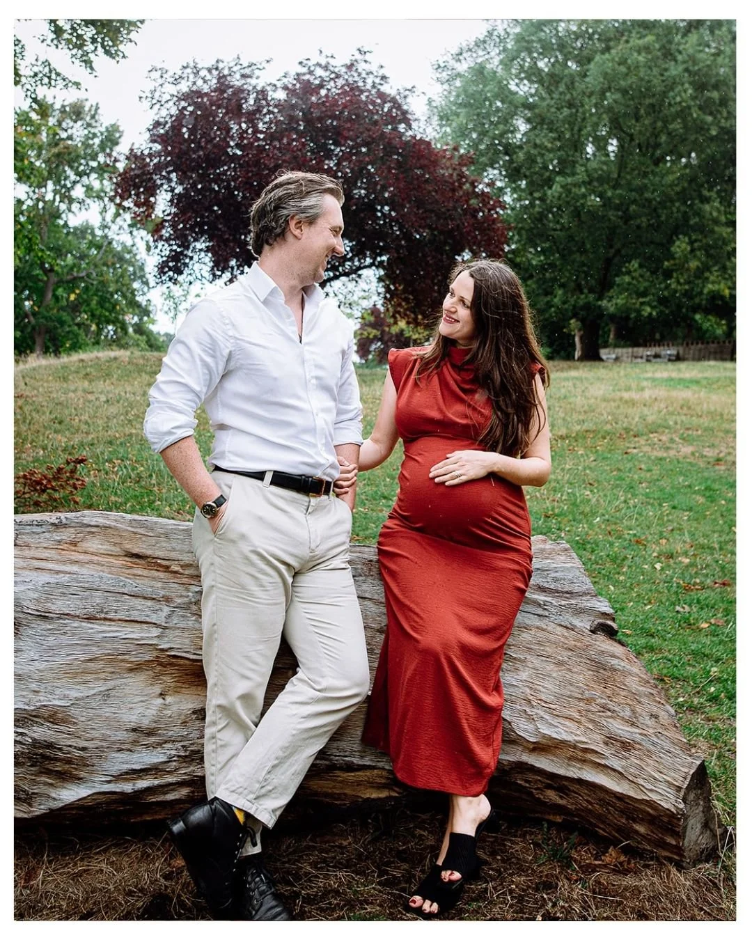 Maternity photoshoot in Herne Hill, South London. Couple looking at each other, sitting in park in rain during outdoor natural lifestyle maternity photoshoot.