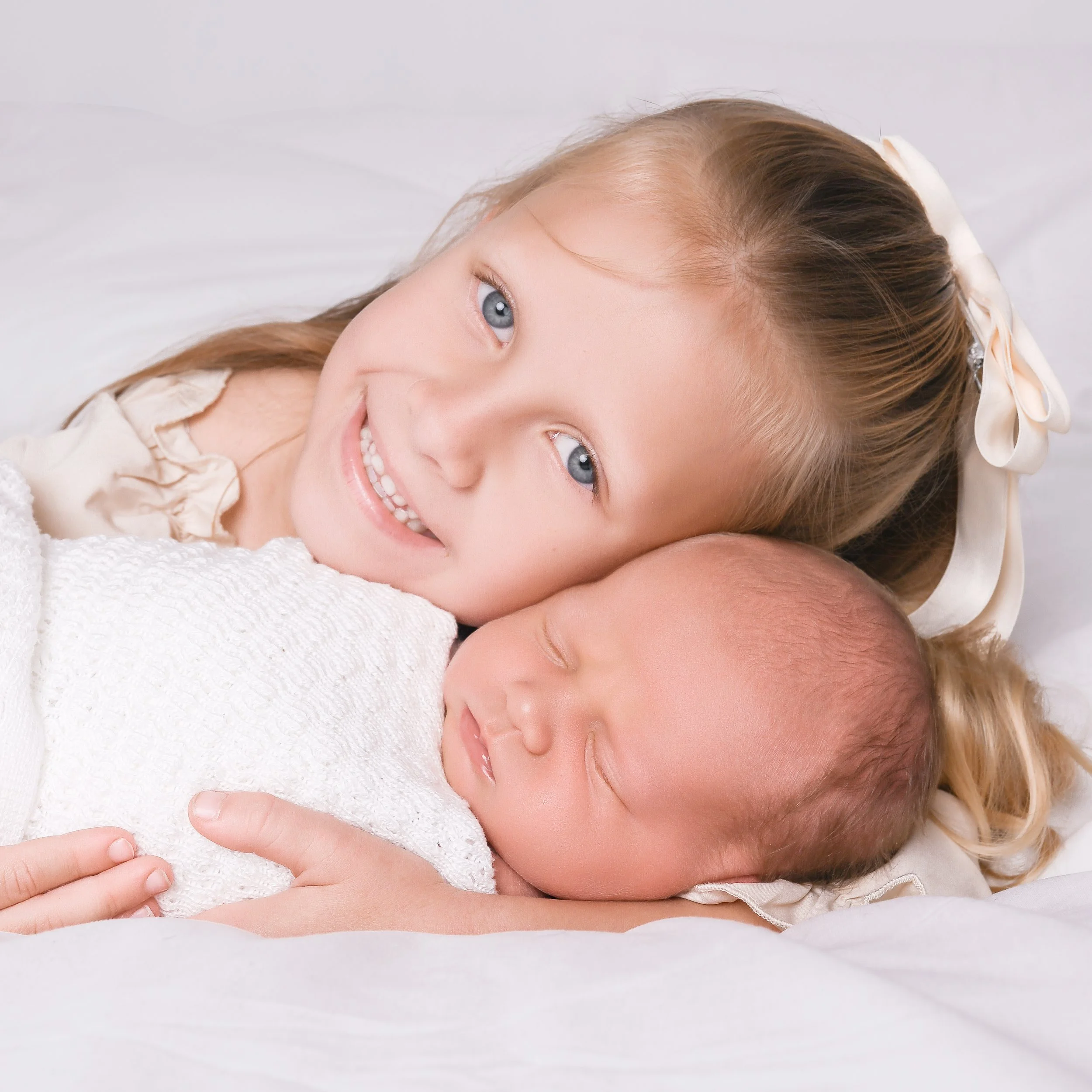 Big sister holding baby brother in a newborn photoshoot. bright eyes and beautiful baby wrap